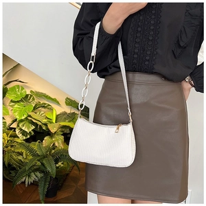 Close-up of white woven underarm bag featuring gold zipper and stylish chain strap detail