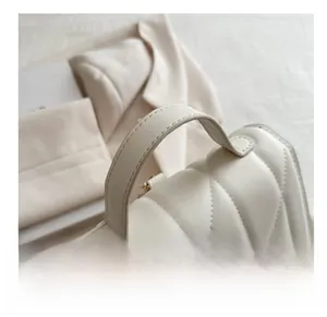 Detail shot of beige quilted handbag featuring arc handle and elegant golden hardware