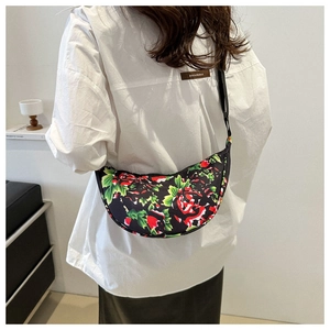 Rear view of model wearing a black floral crescent crossbody bag with red and green patterns