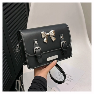 Detail of black crossbody bag with silver bow buckle and white contrast stitching