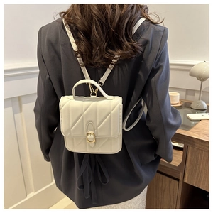 Detail of white quilted mini backpack with gold buckle and leather handle on a grey blazer