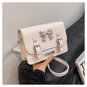 Detail view of cream PU leather crossbody bag featuring silver metal bow and double buckles