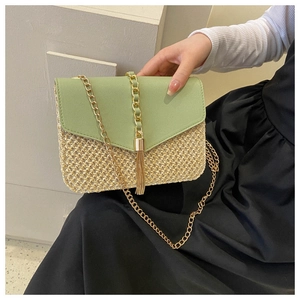 Detail of straw crossbody bag with green leather flap and golden tassel charm