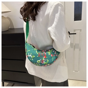 Model wearing a vibrant green floral crescent bag with adjustable shoulder strap over white blazer