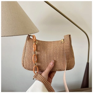 Close-up of straw woven crescent bag with vibrant orange acrylic chain and hand detail