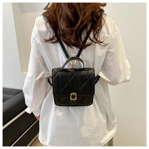 Rear view of a model wearing a black quilted mini backpack with a gold square clasp