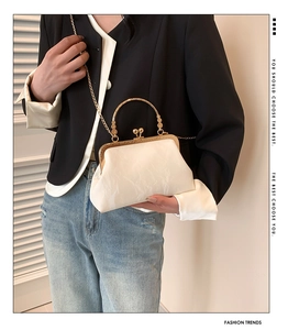Close-up of white cloud-textured handbag with gold metal frame and pearl handle detail