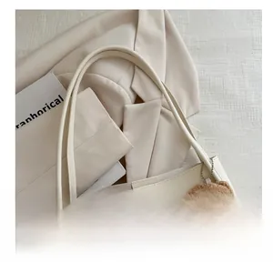 Detail of off-white faux leather tote bag with thin straps and a brown plush bear charm