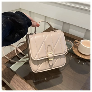 Detail of beige quilted leather crossbody bag with gold buckle on wooden table