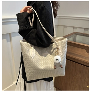 Gros plan sur un sac cabas blanc tissé avec une breloque en peluche et des bretelles simples
