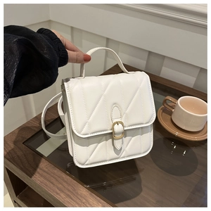 Close-up of white quilted handbag with golden buckle on a wooden side table