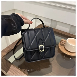 Close-up of black quilted leather handbag with gold buckle detail on a wooden table