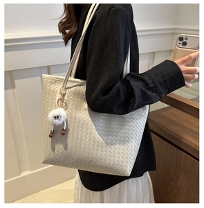 Détail d'un cabas tressé beige orné d'un adorable pendentif en peluche blanc