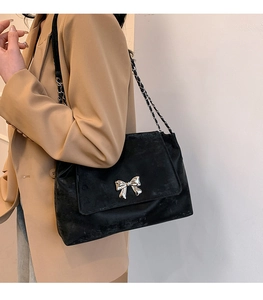 Close-up of black velvet shoulder bag with silver bow buckle and chain strap on a model