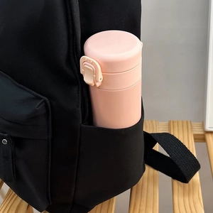 Détail d'une poche latérale de sac à dos noir contenant une gourde rose sur un support