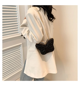 Detail of glitter butterfly crossbody bag with gold chain worn on white blazer