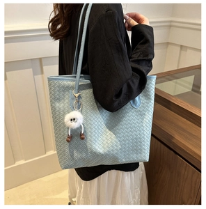 Vue détaillée du sac cabas tissé bleu clair avec un joli pendentif monstre en peluche blanc