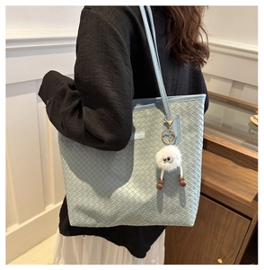 Détail du cabas en cuir tressé bleu clair avec un adorable charm monstre en peluche blanc