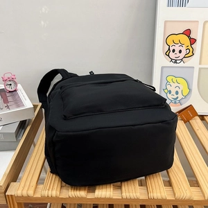 Sac à dos noir minimaliste sur étagère en bois avec des livres et un réveil matin