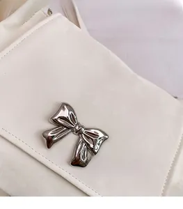 Detail of white leather shoulder bag featuring a silver metal bow clasp and neat stitching
