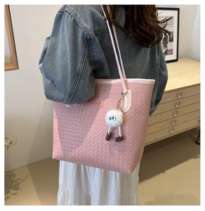 Sac cabas rose tressé avec breloque en peluche blanche porté par un mannequin femme