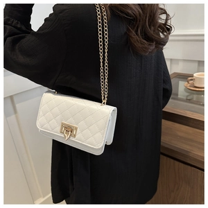 Détail d'un sac matelassé blanc avec un fermoir tournant doré et une fine bandoulière chaîne