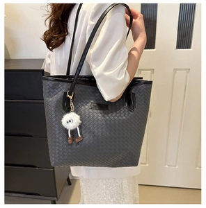 Détail du sac cabas tressé gris foncé avec breloque peluche et bandoulière noire longue