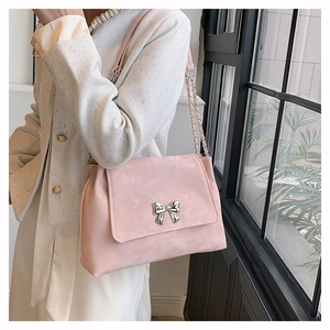 Detail of pink shoulder bag featuring a silver metal bow buckle and chain strap on model