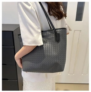 Détail d'un sac cabas tressé gris avec écusson logo noir et bandoulière chic