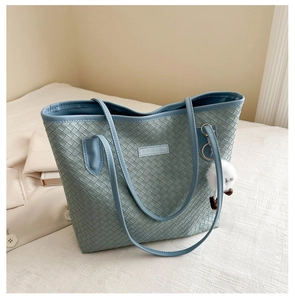 Détail du sac cabas bleu clair tressé avec logo et breloque pompon blanc élégant