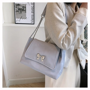 Fashionable light blue shoulder bag with golden bow clasp shown on a model side view