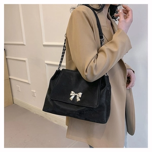 Detailed side view of black velvet handbag featuring silver bow buckle and chain strap