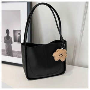 Detail of minimalist black leather tote bag with a brown plush clown charm on a white stand