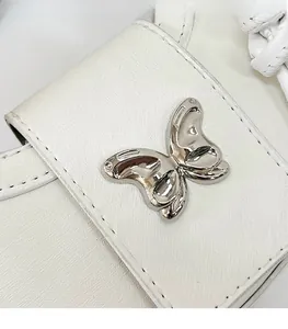 Détail du sac en cuir blanc avec boucle métallique en forme de papillon argenté