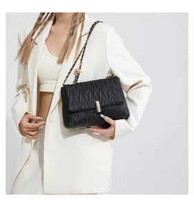 Detail of black pleated chain shoulder bag with gold metal clasp on a white suit