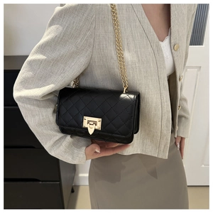 Détail du sac bandoulière matelassé noir avec chaîne dorée porté sur un blazer beige chic