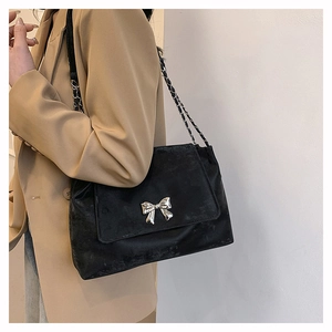 Detailed close-up of a black textured shoulder bag with a silver metal bow and chain strap
