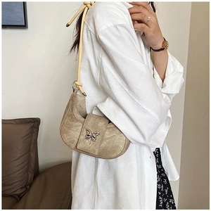 Sac bandoulière demi-lune kaki avec papillon argenté porté sur une chemise blanche