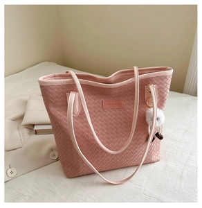Détail d'un sac cabas tressé rose avec un pompon en fourrure blanche sur tissu doux