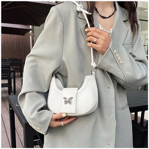 Détail du sac selle blanc avec boucle papillon argentée sur un blazer vert sauge