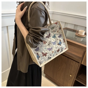 Detailed close-up of a beige woven tote bag featuring colorful butterfly embroidery accents