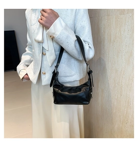 Detail of soft black leather underarm bag with silver zipper on a white tweed jacket