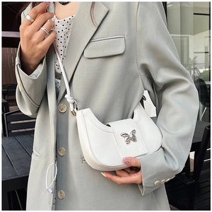 Gros plan d'un sac à bandoulière demi-lune blanc avec une boucle papillon argentée