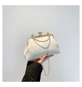 Close-up of white satin evening bag with golden metal handle and elegant texture