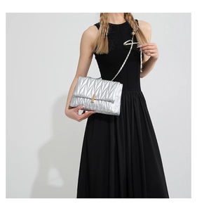 Silver quilted crossbody bag with gold chain strap shown on black dress