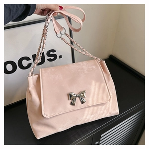 Detail of pink shoulder bag showing a silver metal bow buckle and chain strap