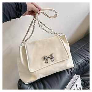 Detailed shot of cream faux leather shoulder bag with silver bow buckle and chain strap