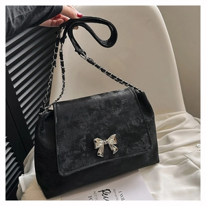 Close-up of a black vintage shoulder bag featuring a silver metal bow and chain strap