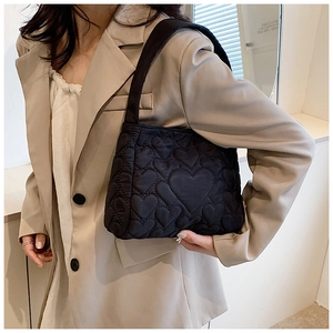 Detailansicht der schwarzen Tragetasche mit Herzsteppmuster und beigem Blazer