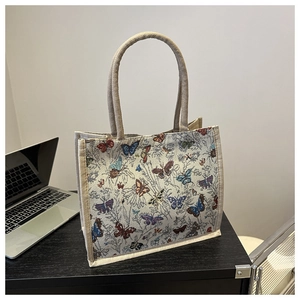 Detail of woven beige tote bag featuring colorful butterfly patterns and thick handles